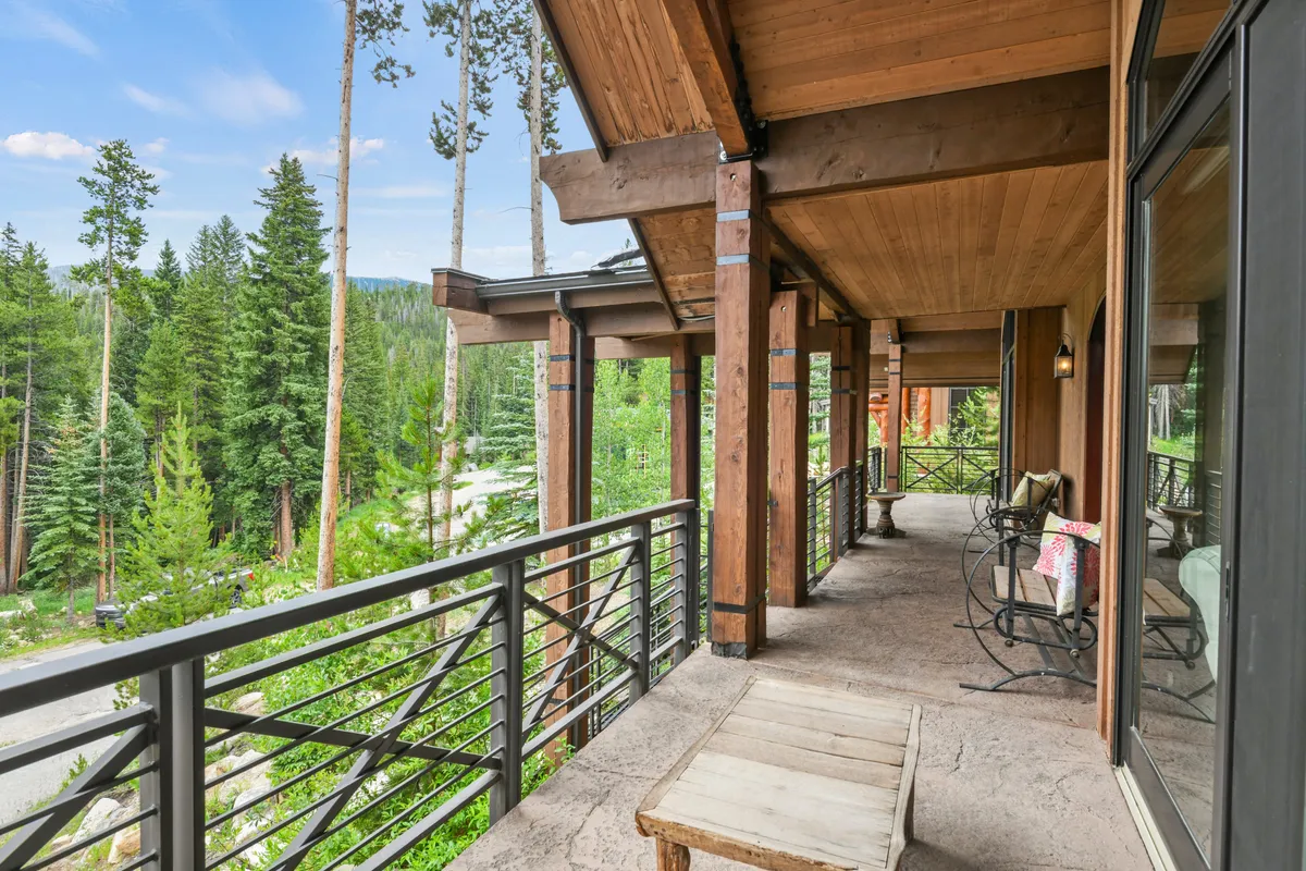A serene wooden deck framed by metal railings, perched above a forested landscape with sweeping mountain views. The deck offers comfortable space for relaxing, reading, or gathering with friends while taking in the scenery.