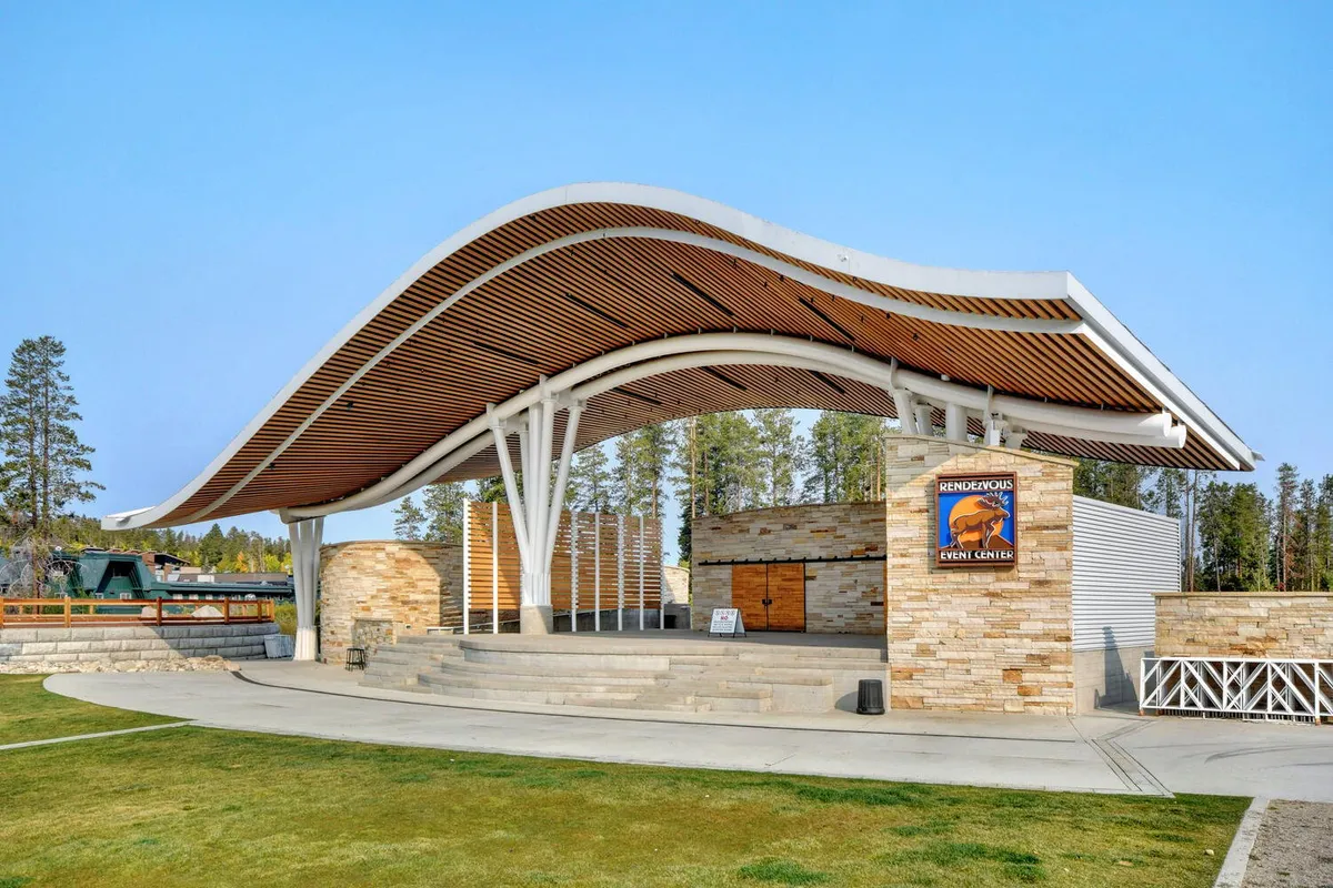 An exterior shot of the Hideaway Park Amphitheater, featuring its distinctive curved roof, stone facade, and open stage area. The image evokes the atmosphere of community concerts, festivals, and outdoor gatherings under the stars.