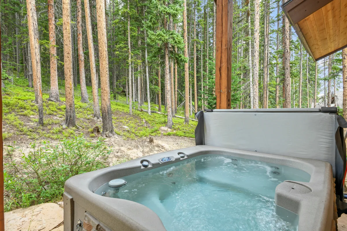 An exterior shot of a private hot tub, surrounded by tall trees and natural landscape. The setting is tranquil and immersed in nature, perfect for unwinding after adventure-filled days.