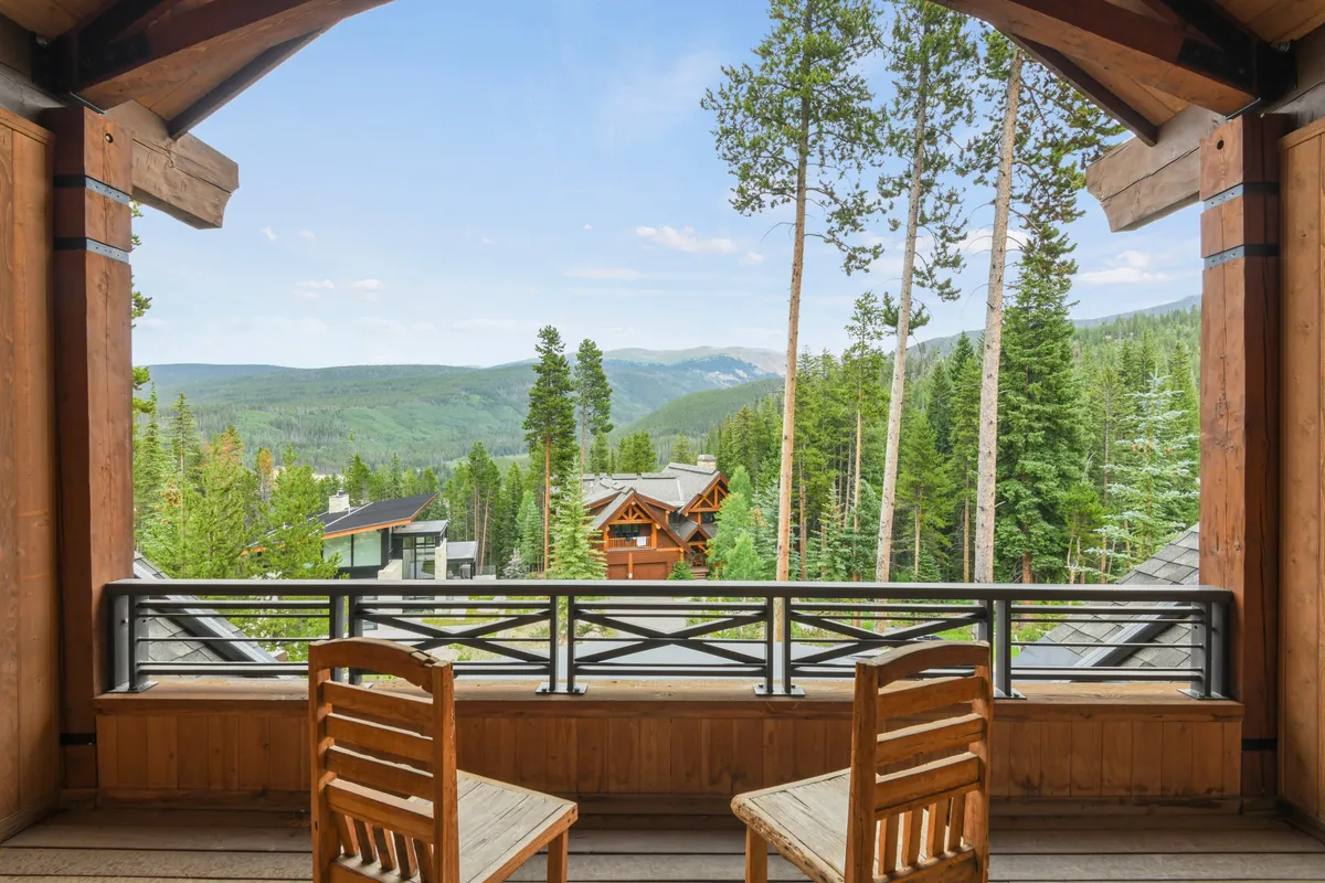 A tranquil balcony with wooden chairs overlooks a breathtaking mountain view surrounded by tall trees, inviting guests to relax, spot wildlife, or enjoy a morning coffee immersed in nature.