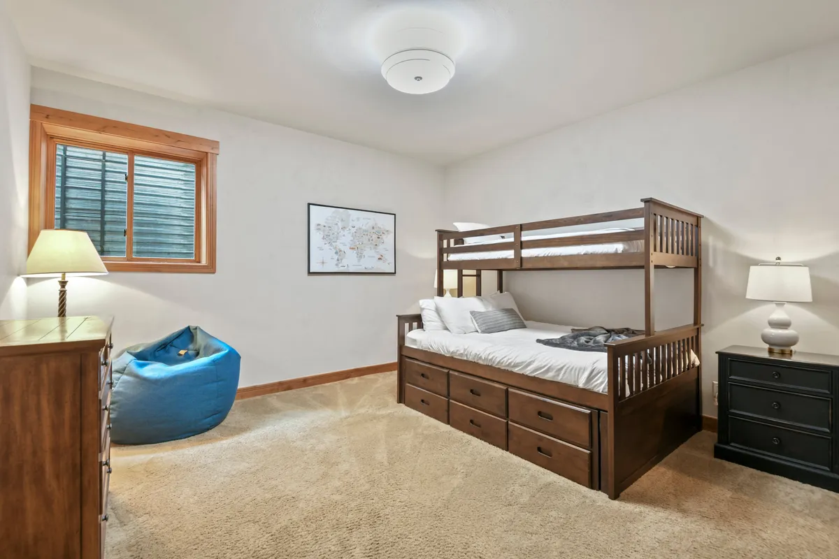 A fun and inviting bedroom designed for children, featuring a twin-over-queen bunk bed with a trundle, a soft bean bag chair, and playful lighting. The cozy atmosphere is enhanced by a map on the wall—great for family sleepovers or kid-friendly stays.