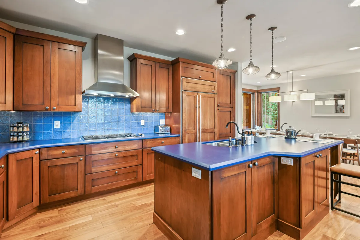 The kitchen is showcased from another angle, featuring stylish blue countertops, warm wooden cabinetry, stainless steel appliances, and elegant pendant lighting. The mood is inviting and sets the scene for both casual breakfasts and lavish dinners.