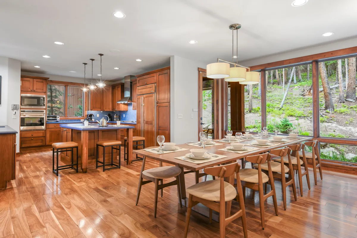 This image highlights an expansive dining area adjacent to an island kitchen, with a large table capable of seating a group. Floor-to-ceiling windows fill the space with light, creating an inviting backdrop for shared meals and celebrations.